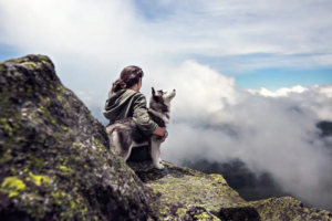 Eine Frau sitzt auf einem Berg und hält ihren Husky im Arm