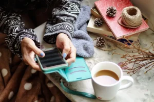 Ein Handy wird in der Hand gehalten, daneben steht eine Tasse mit Kaffee