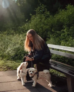 Eine Frau sitzt auf einer Bank - vor ihr zwei Maltipoos